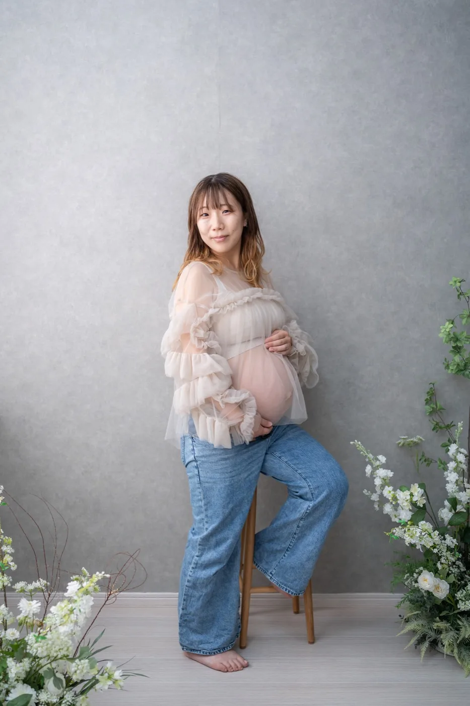 グレーの背景でスツールに寄りかかる、チュール衣装の妊婦