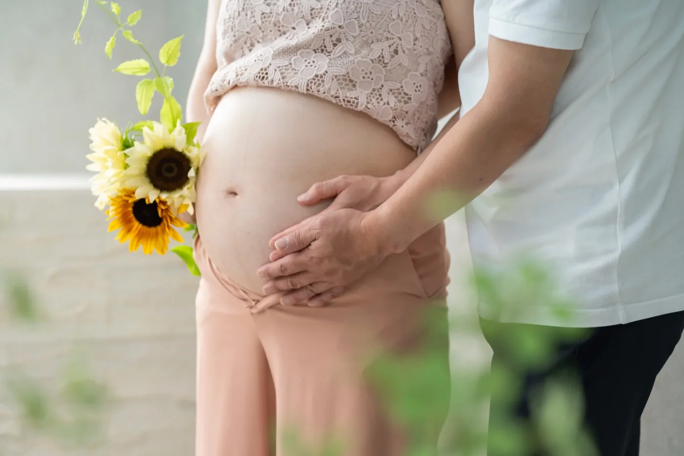 ひまわりを持つおなかに、夫婦で手を添えたマタニティフォト