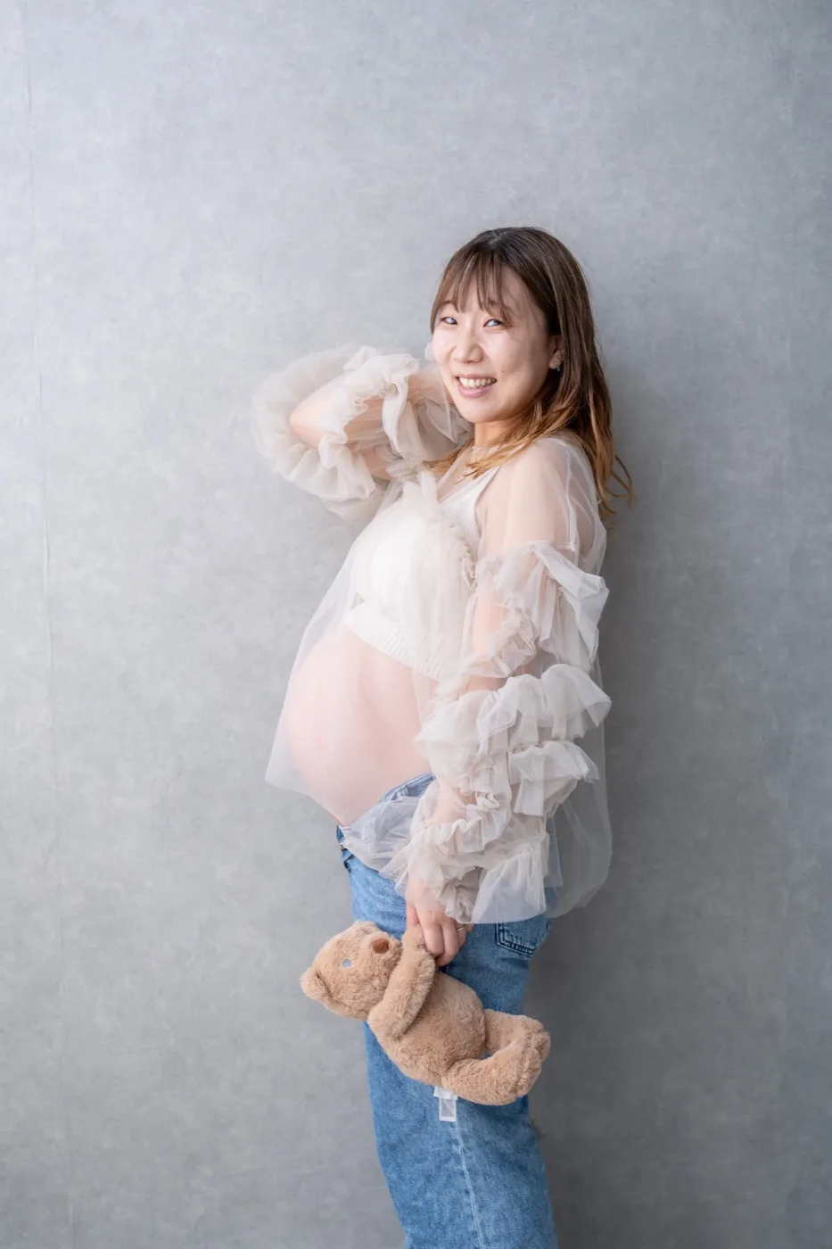 チュールの衣装でくまのぬいぐるみを持ち、こちらを見て笑う妊婦