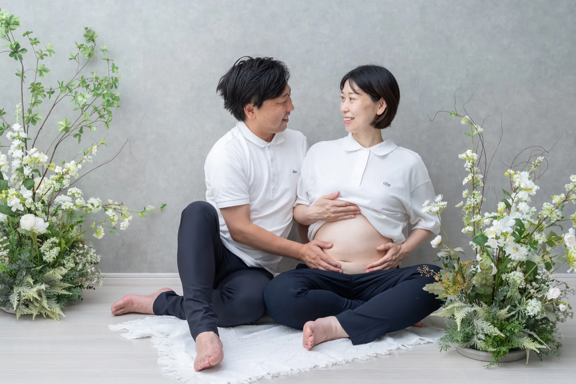 グリーンに囲まれた床に座り、おなかに手を添える夫婦